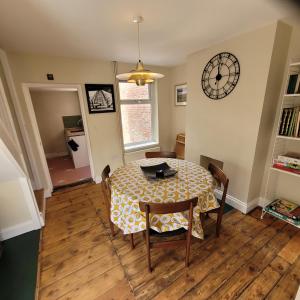 a dining room table with chairs and a clock on the wall at Pea Cottage in Kessingland