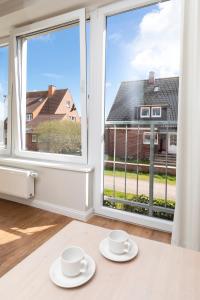 two white cups and saucers on a table in front of a window at Haus Delft Elisa in Juist