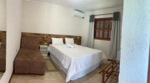 1 dormitorio con 1 cama blanca y 1 silla en Vinha dos Lagos Hotel, en Rancho Queimado
