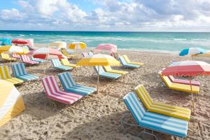 un grupo de sillas y sombrillas en una playa en The Confidante Miami Beach, part of Hyatt, en Miami Beach