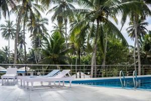 a pool with white lounge chairs and palm trees at Marine Palace Beach Hotel in Kovalam