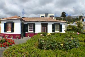 a white house with black shuttered windows and flowers at Casa da Avó Benvinda in Funchal