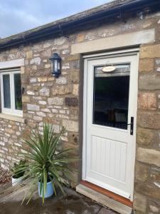 a stone house with a white door and a plant at The Annexe in Middleham