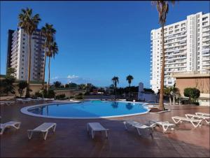 una piscina con sillas, palmeras y edificios en Tenerifeopenhome Club Paraiso, en Adeje