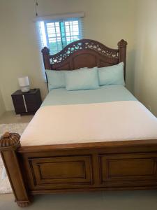 Bett mit einem Holzrahmen und einer weißen Matratze in der Unterkunft Three Palm Villa in Montego Bay