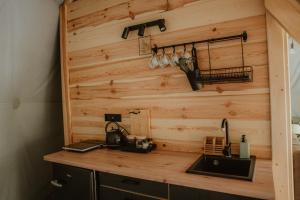 a kitchen with a wooden wall and a counter with a sink at Czarna Hańcza Glamping in Głęboki Bród
