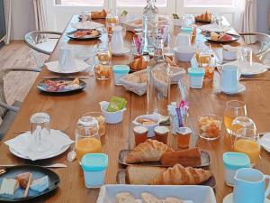 uma longa mesa de madeira com pratos de comida e bebidas em Les Rêves de Baie de Somme Chambres d'hôtes , Table d'hôtes et Spa em Béhen