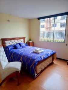 a bedroom with a bed with a blue comforter and a window at Amplio apartamento El Eden cerca Embajada Americana y Solca - zona tranquila seguridad 24-7 in Quito
