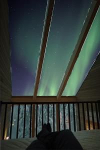 une personne assise sur un lit qui regarde les lumières du nord dans l'établissement Villa Auroras Pöllö, à Syöte