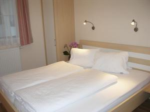 Bett mit weißer Bettwäsche und Kissen in einem Zimmer in der Unterkunft Apart Ahorn in Finkenberg