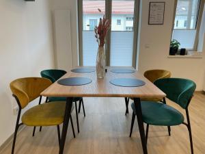 einen Holztisch mit grünen Stühlen und eine Vase aus Blumen in der Unterkunft LIGHTPLACE • Design • Boxspring • Balkon • 2 Smart TV •Innenstadt in Braunschweig