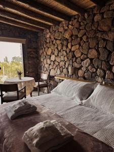 sypialnia z kamienną ścianą z łóżkiem i stołem w obiekcie Bendita Piedra Suites, Las Compuertas Lujan de Cuyo w mieście Lujan de Cuyo