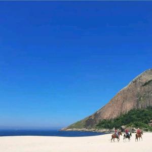 um grupo de pessoas andando a cavalo na praia em Recanto Ganesha seu paraíso na praia, no Recanto de Itaipuaçu ao lado de Itacoatiara em Itacoatiara