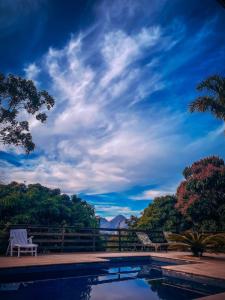 a swimming pool with two chairs and a sky at Pousada Alto Itaipava in Itaipava