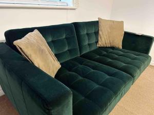 Un sofá de cuero verde con dos almohadas. en East London Apartment near Station & Free Parking, Arcade Machine, en Romford