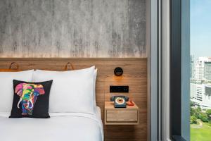 a bed with a pillow and a clock next to a window at Moxy Bangkok Ratchaprasong in Bangkok