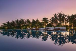 a pool with chairs and palm trees at dusk at The Riviera Maya EDITION at Kanai in Playa del Carmen