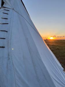 a close up of a white tent with the sunset in the background at JMA Tipi in Riverton