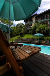 a wooden bench next to a swimming pool with umbrellas at Paraíso Hostel Praia do Rosa in Praia do Rosa