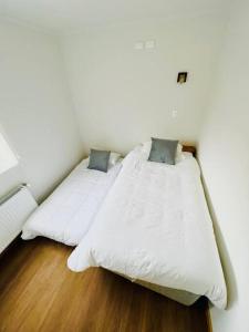 1 dormitorio con 2 camas, sábanas blancas y suelo de madera. en Departamento duplex 4, en Puerto Natales