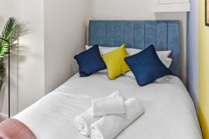 een wit bed met blauwe en gele kussens bij Stylish and Snug Studio in Enfield