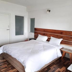 a bedroom with a large white bed with a wooden headboard at Aaravi Garden Homestay in Kalimpong