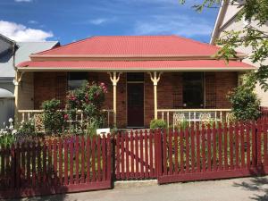 Melville Heritage Cottage, Hobart CBD في هوبارت: سياج أحمر أمام منزل بسقف أحمر
