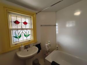 Melville Heritage Cottage, Hobart CBD في هوبارت: حمام مع حوض ونافذة مع ورود حمراء +16 صورة