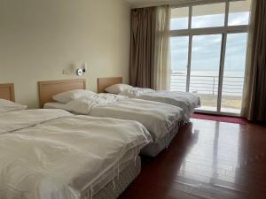 three beds in a hotel room with a large window at 馬港驛站 Oldharbor Hostel in Nangan