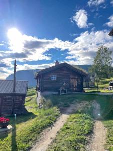 a wooden house on a field with a dirt road at Stallen - koselig lite hus på gårdstun in Skjåk