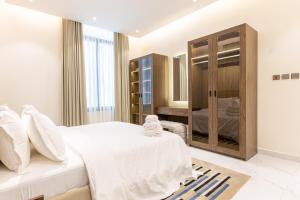 Amber Hospitality - Al Qairawan في الرياض: غرفة نوم بسرير أبيض وخزانة خشبية
