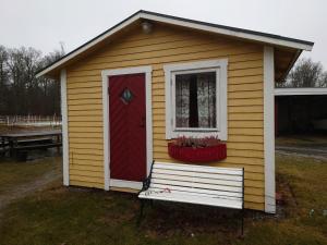 una pequeña casa con una puerta roja y un banco en Lilla Röaby, en Bräkne-Hoby