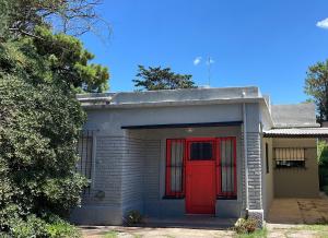 una puerta roja en una pequeña casa con un árbol en Playa Quequén en Quequén