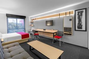 a hotel room with a bed and a desk and a table at City Express Plus by Marriott Guadalajara Expo in Guadalajara