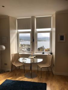 a room with a table and two chairs and two windows at Millport Beach Apartment, Crichton St, sea views in Millport