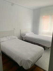 two beds in a room with white sheets at Apartamento en Liencres in Liencres