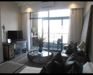 a living room with a couch and a table and a desk at The Trilogy,Menlyn Maine in Pretoria