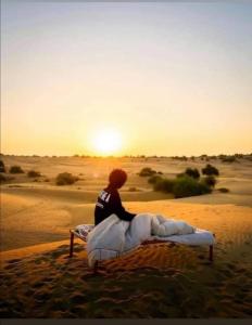 Ein Mann auf einem Bett in der Wüste in der Unterkunft Desert Safari Jaisalmer in Sām