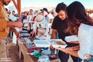 a group of people standing around a table with food at flamingo camp in Dār as Salām