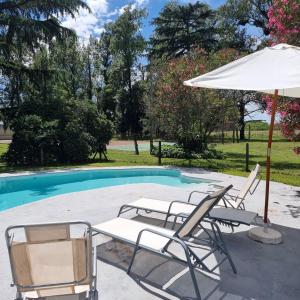 eine Gruppe Stühle und ein Sonnenschirm neben einem Pool in der Unterkunft La Centenaria, casa de campo in Bragado