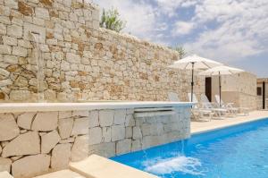 uma piscina com um guarda-sol ao lado de uma parede de pedra em Villa Dolce Valle em Ragusa