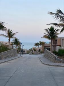 an empty street with palm trees and the ocean at Sifah Beach Cottage in As Sīfah