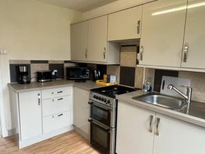 a kitchen with white cabinets and a stove and a sink at Above the harbour wick in Wick