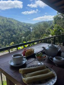 a table with a breakfast of coffee and fruit on a balcony at Divine View Homestay in Ella