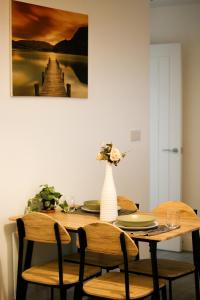 a wooden table with chairs and a vase with flowers at The Madison Apartment by GGE, Hemel Hempstead Town Centre, Contractors Welcome, Sleeps 6 in Hemel Hempstead