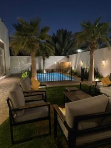 un patio con 2 sillas, una mesa y palmeras en شاليه لونار, en Unaizah