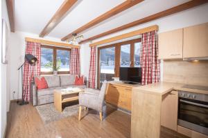 a living room with a couch and a kitchen with windows at Alpenherz Ferienwohnungen in Pertisau