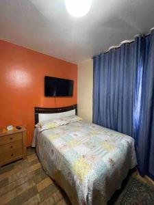 een slaapkamer met een bed met blauwe gordijnen en een televisie bij Casa em frente a Praia das Dunas, Cabo Frio - RJ in Cabo Frio
