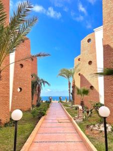 a red brick path between two buildings with palm trees at Dar Mustapha in Sidi Ifni