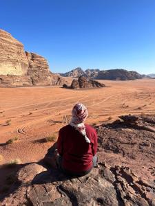 a person sitting on a rock in the desert at wadi rum caeser camp in Wadi Rum